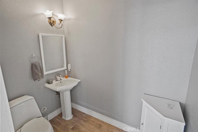 half bath with baseboards, toilet, and wood finished floors