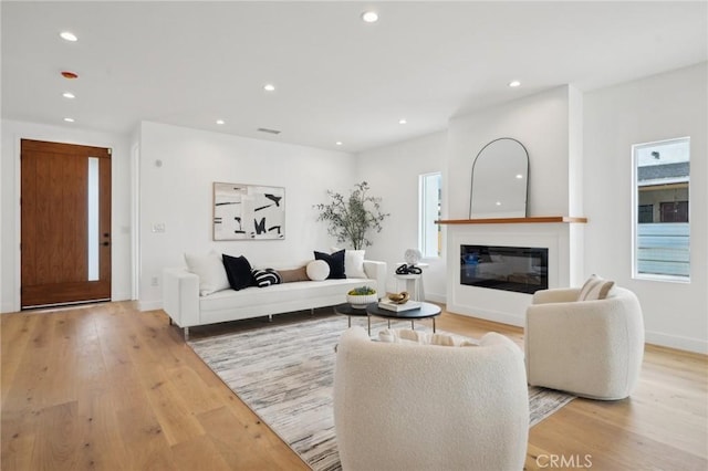 living room featuring visible vents, baseboards, a glass covered fireplace, recessed lighting, and light wood finished floors