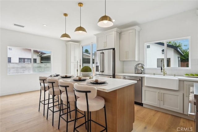 kitchen featuring decorative backsplash, appliances with stainless steel finishes, a center island, a sink, and visible vents