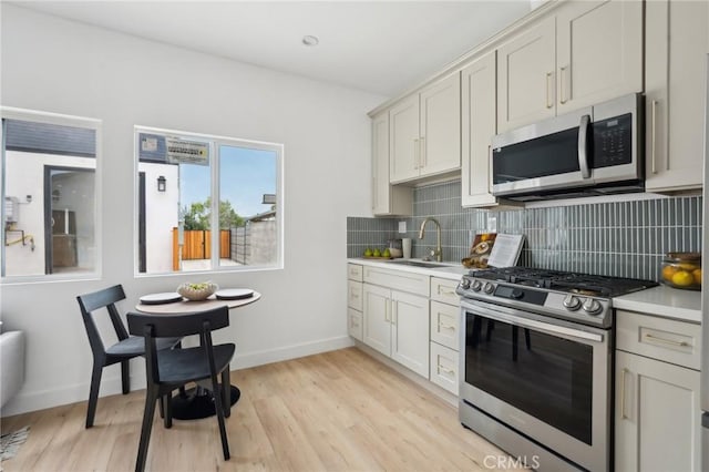 kitchen with a sink, tasteful backsplash, stainless steel appliances, and light countertops