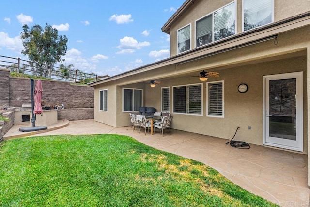 rear view of property with stucco siding, fence, ceiling fan, a patio, and a lawn