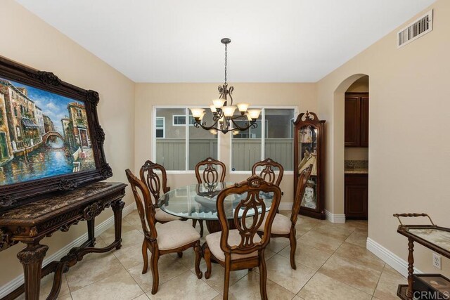 dining area featuring arched walkways, light tile patterned floors, baseboards, visible vents, and a notable chandelier
