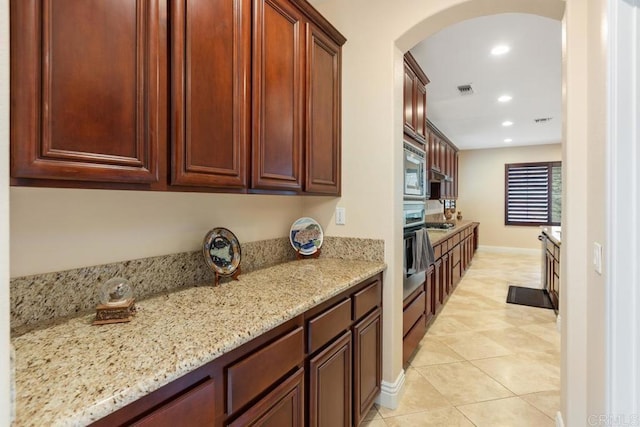kitchen with recessed lighting, light tile patterned floors, light stone counters, arched walkways, and appliances with stainless steel finishes