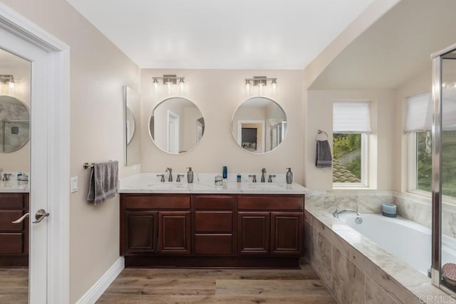 full bath with double vanity, wood finished floors, a bath, and a sink