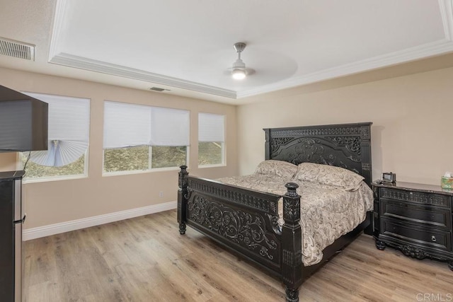bedroom with visible vents, light wood-type flooring, a tray ceiling, and baseboards