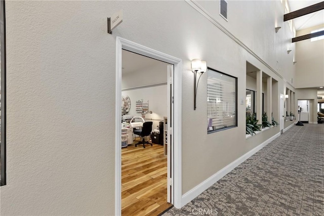 corridor featuring visible vents, baseboards, and a textured wall