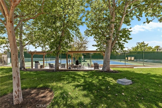 view of property's community with fence, a tennis court, and a yard