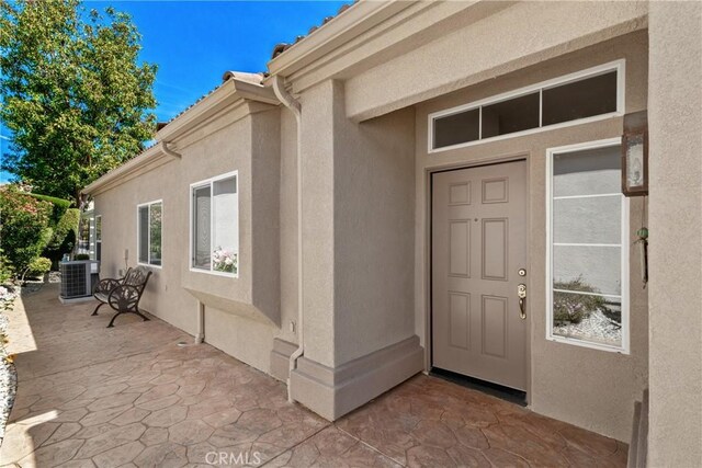doorway to property with stucco siding, a patio area, and central AC