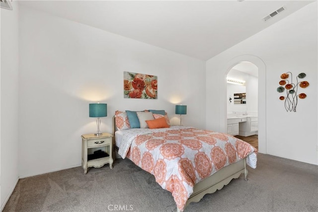 bedroom with arched walkways, visible vents, light carpet, and ensuite bath
