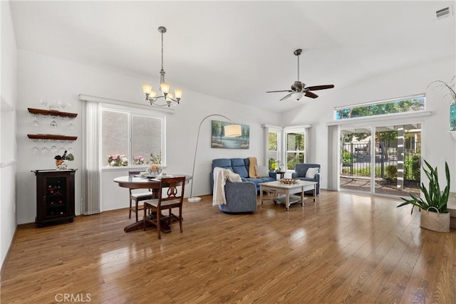 living room with wood-type flooring, ceiling fan with notable chandelier, visible vents, and vaulted ceiling