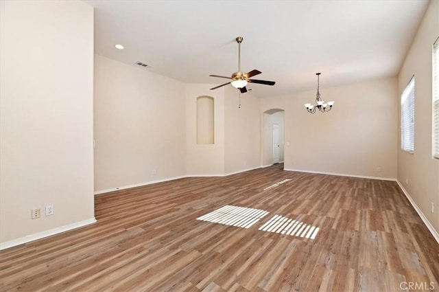 unfurnished living room with visible vents, light wood-style floors, baseboards, arched walkways, and ceiling fan with notable chandelier