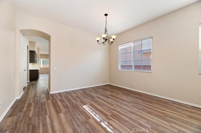 spare room featuring a chandelier, baseboards, wood finished floors, and arched walkways