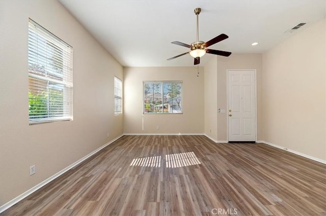 unfurnished room with a wealth of natural light, wood finished floors, ceiling fan, and visible vents