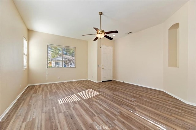empty room featuring wood finished floors, ceiling fan, visible vents, and baseboards