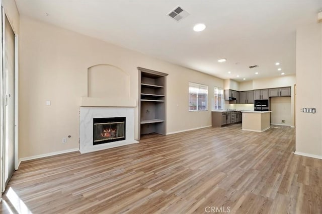 unfurnished living room with visible vents, baseboards, light wood finished floors, a premium fireplace, and built in shelves