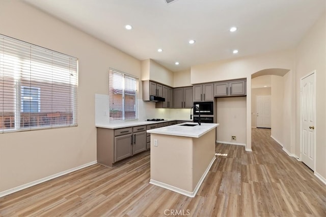 kitchen featuring gray cabinets, arched walkways, light wood-type flooring, and black appliances