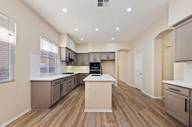 kitchen with visible vents, gray cabinetry, under cabinet range hood, arched walkways, and gas cooktop