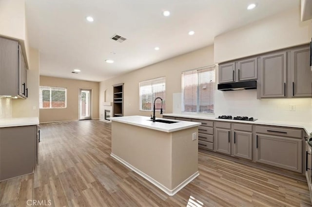 kitchen featuring black cooktop, gray cabinetry, under cabinet range hood, and a sink
