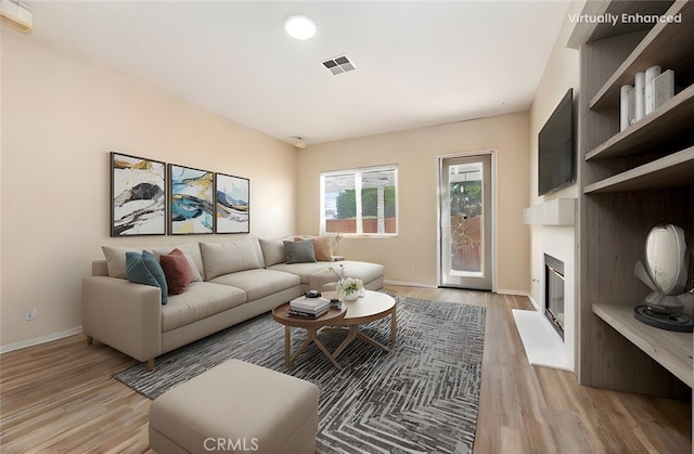 living area with a fireplace with flush hearth, visible vents, baseboards, and light wood-style floors