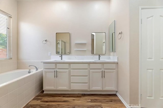 bathroom featuring double vanity, wood finished floors, a bath, and a sink