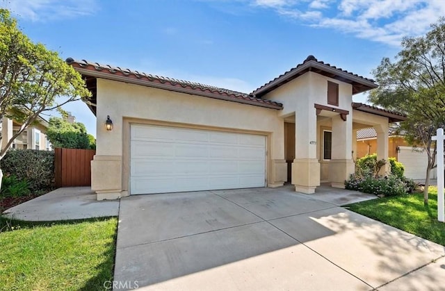 mediterranean / spanish home with a garage, driveway, a tiled roof, stucco siding, and fence