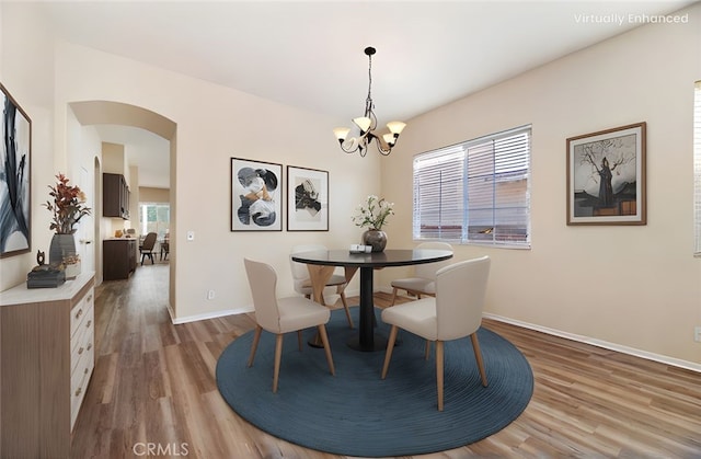 dining room with arched walkways, an inviting chandelier, baseboards, and light wood-type flooring
