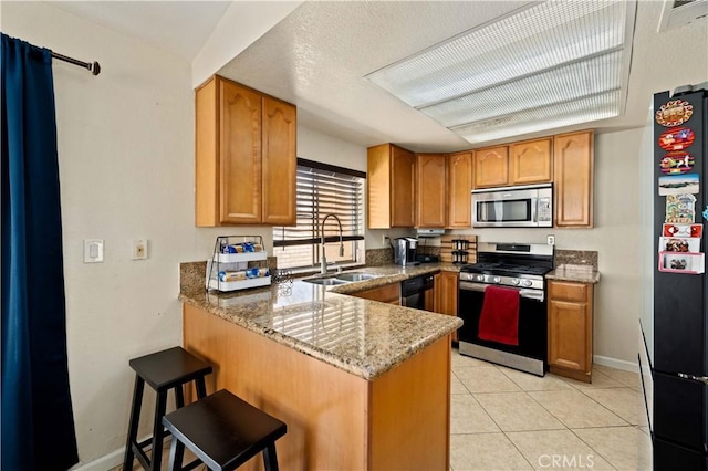 kitchen with black appliances, stone counters, a sink, baseboards, and a peninsula