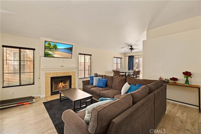living room featuring a tiled fireplace, baseboards, ceiling fan, and light wood-style floors