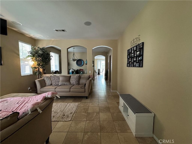 tiled living area featuring a healthy amount of sunlight, visible vents, and arched walkways