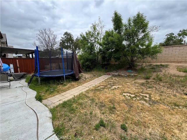 view of yard with a trampoline, a patio area, and fence