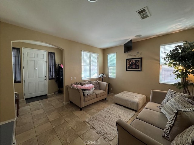 living room with light tile patterned floors, arched walkways, visible vents, and baseboards