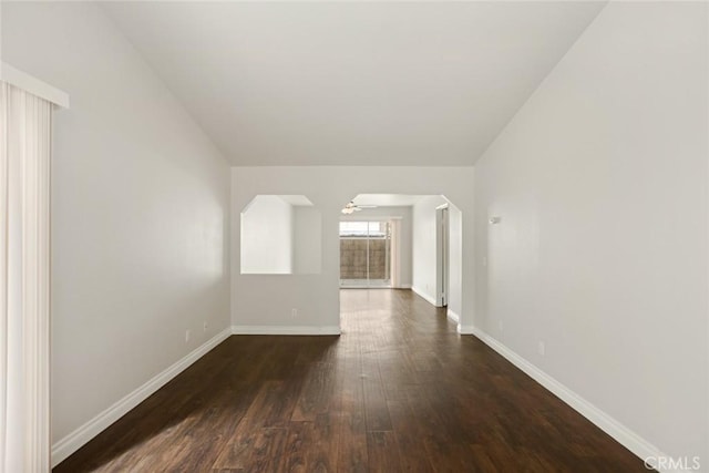 unfurnished room with baseboards, dark wood-style flooring, and arched walkways