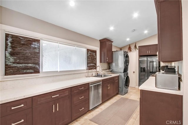 kitchen featuring stacked washer and dryer, dark brown cabinets, a sink, lofted ceiling, and stainless steel appliances