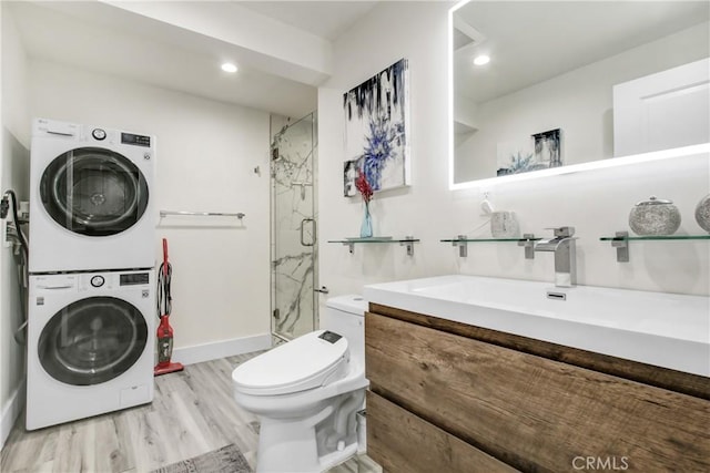 bathroom with vanity, stacked washer and clothes dryer, wood finished floors, toilet, and a marble finish shower