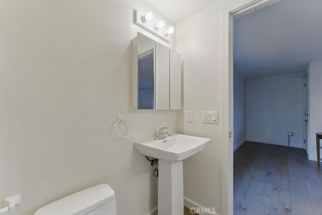 bathroom with a sink, toilet, wood-type flooring, and baseboards