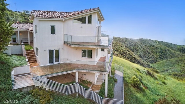 rear view of property featuring stairs, stucco siding, and a tiled roof