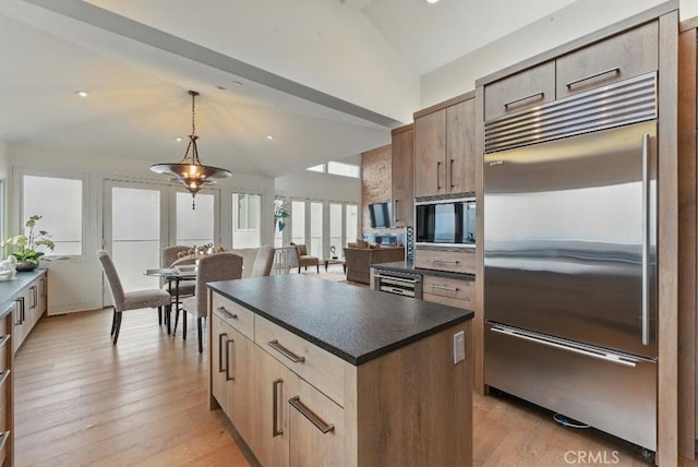 kitchen with light wood-style flooring, built in appliances, dark countertops, a center island, and hanging light fixtures