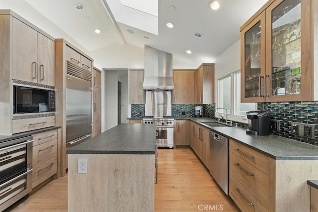 kitchen featuring a sink, built in appliances, dark countertops, lofted ceiling with skylight, and range hood