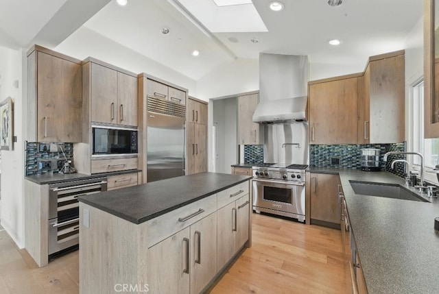 kitchen with a sink, built in appliances, dark countertops, beverage cooler, and wall chimney exhaust hood