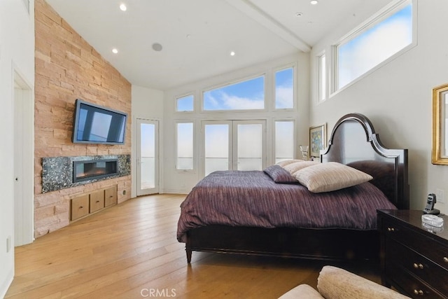 bedroom with a fireplace, light wood finished floors, french doors, and high vaulted ceiling