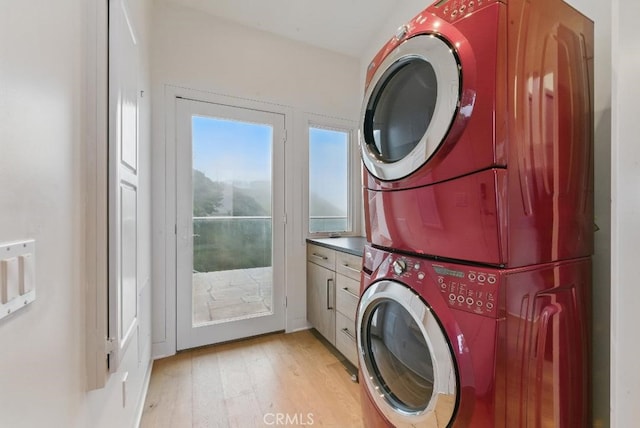 clothes washing area featuring stacked washing maching and dryer, cabinet space, and light wood finished floors