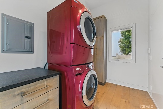 clothes washing area featuring light wood-type flooring, stacked washer / dryer, electric panel, and baseboards