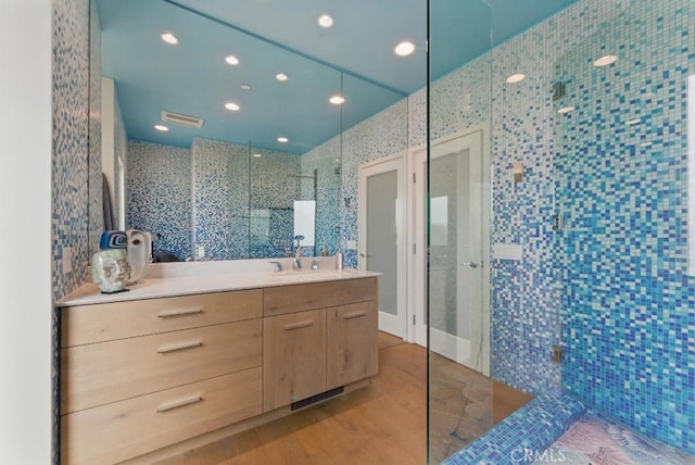 full bathroom featuring recessed lighting, wood finished floors, a walk in shower, tile walls, and vanity