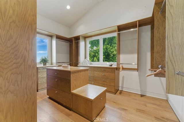 walk in closet with light wood-type flooring and high vaulted ceiling