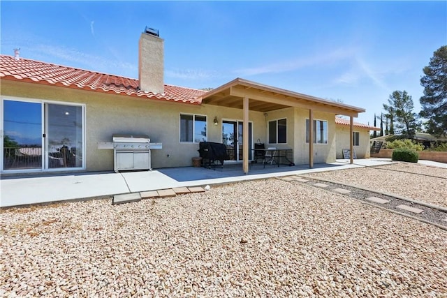 rear view of property with stucco siding, a chimney, a patio area, and a tile roof