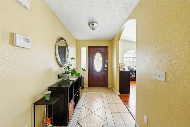 foyer with arched walkways, light tile patterned floors, a textured wall, baseboards, and a textured ceiling