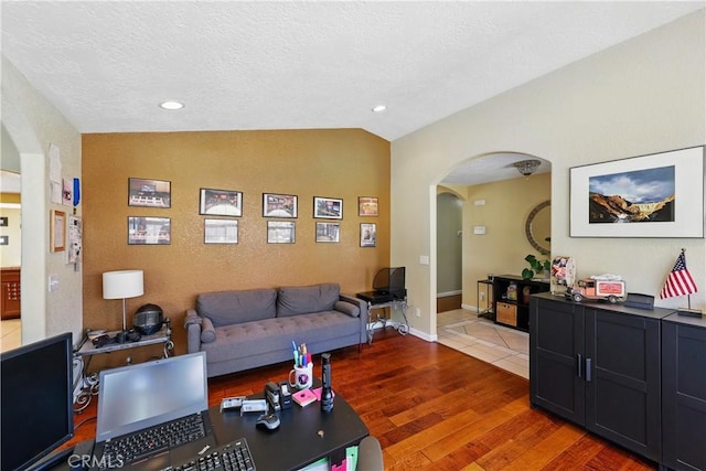 living room featuring recessed lighting, arched walkways, light wood finished floors, a textured ceiling, and lofted ceiling