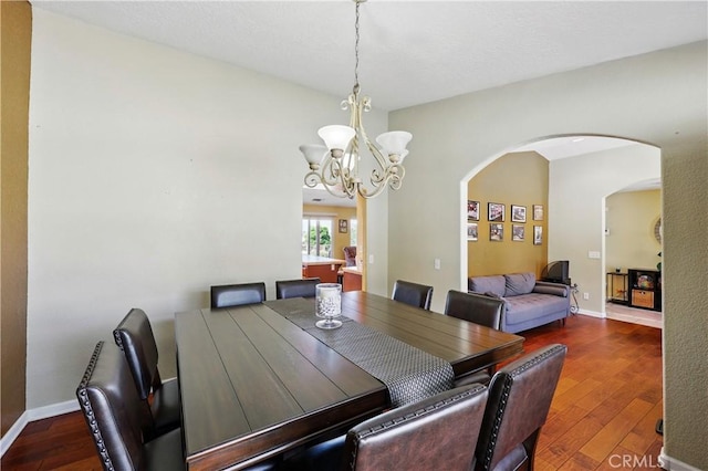dining area with wood finished floors, baseboards, a chandelier, and arched walkways