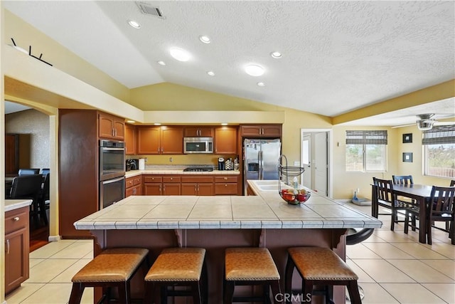 kitchen with a breakfast bar, stainless steel appliances, visible vents, tile countertops, and lofted ceiling