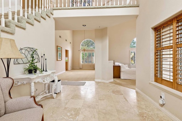 foyer entrance featuring a towering ceiling, carpet flooring, and baseboards